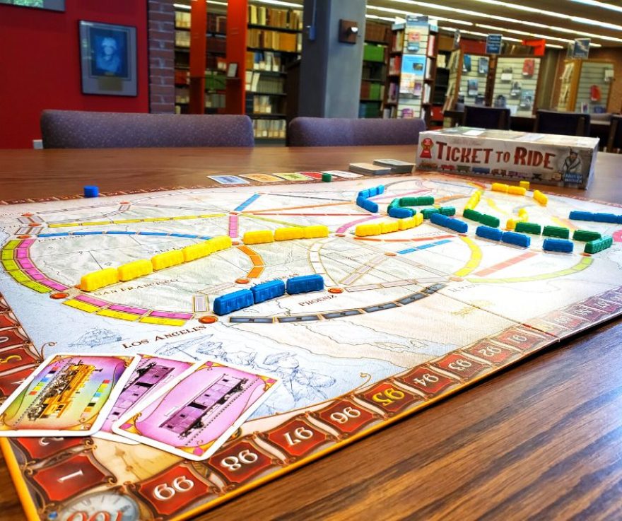 A photo of the game Ticket to Ride mid-play. A board that shows the United States is laid out, and different colored trains are placed on the board. You can see the box in the background