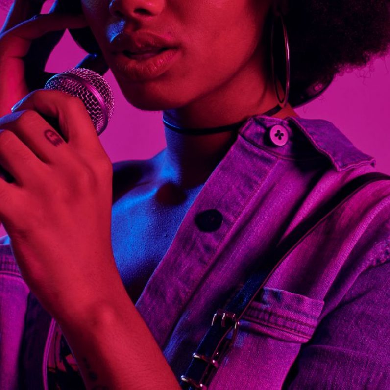 A hazy laser lit photo of a Black woman speaking into a microphone