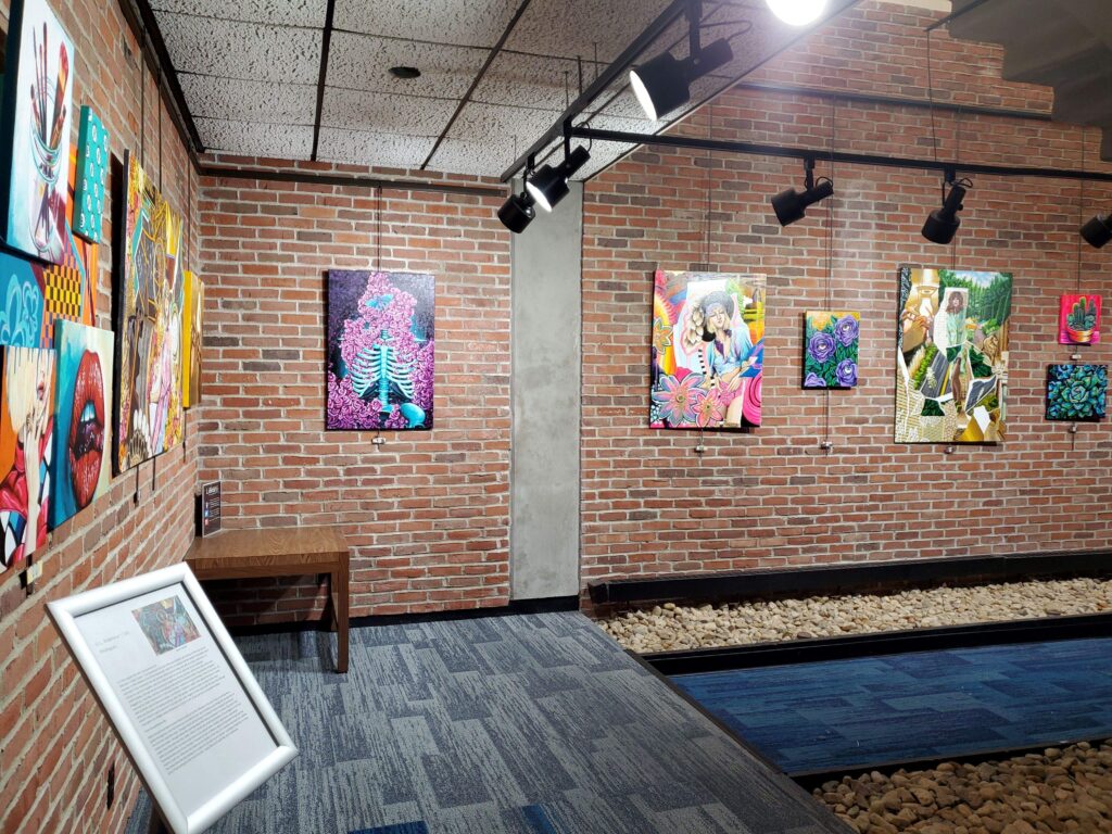 A line of colorful paintings against a brick wall with spotlights shining on them.
