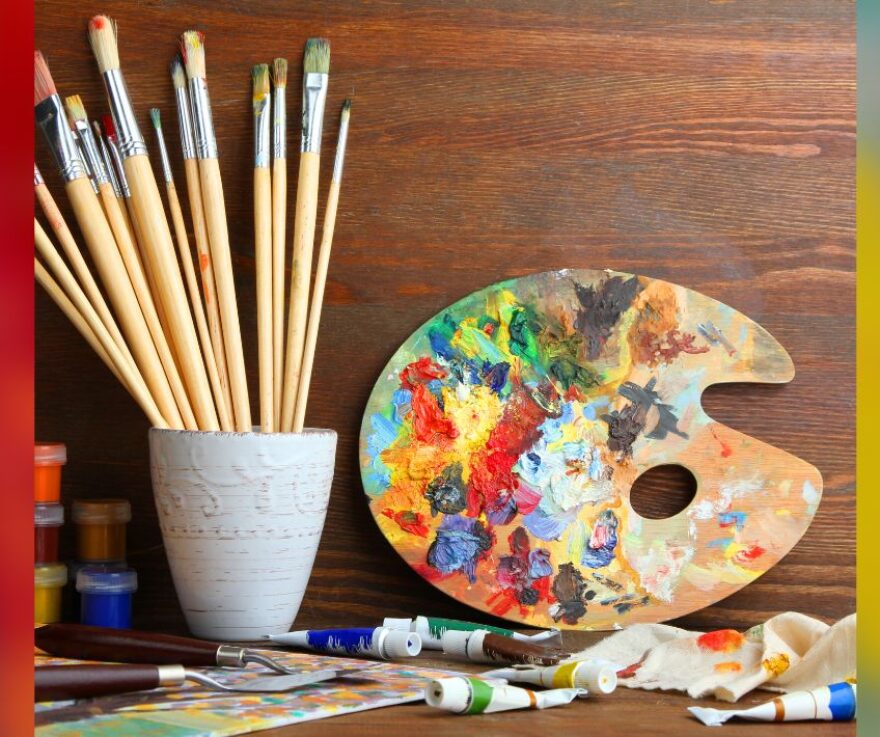 An art palette and a jar full of paint brushes against a wood wall.
