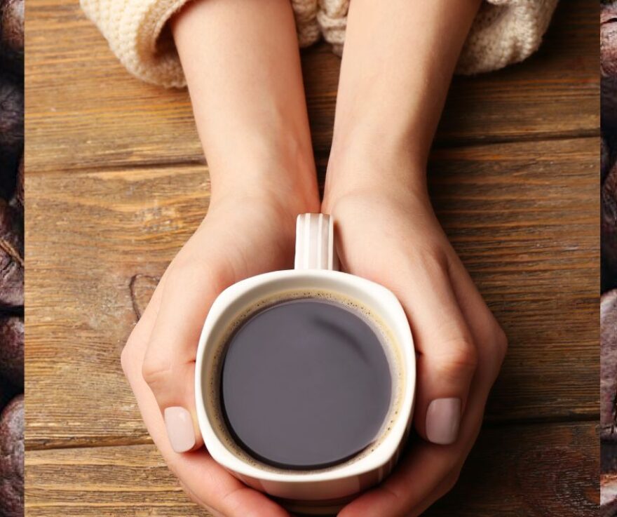 Hands wrapped around a coffee mug. In the background are coffee beans.