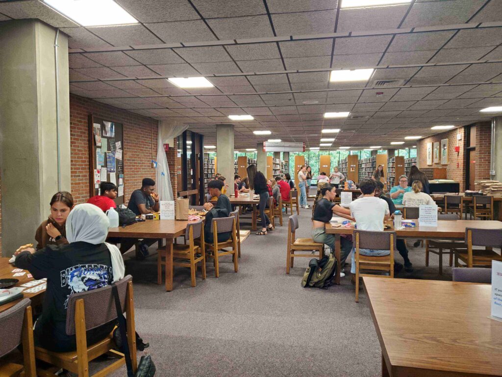 The second floor of the library. There are a lot of wooden tables in the photo, each with a group of students sitting at them, playing games.